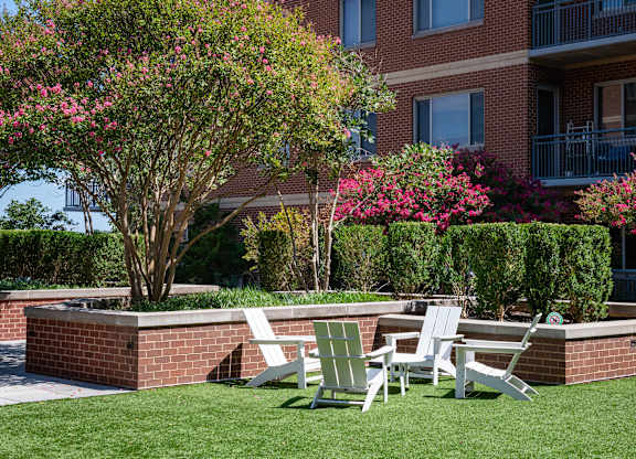 Green courtyard lawn with white Adirondack chairs, flowering trees, trimmed hedges and brick apartment balconies.