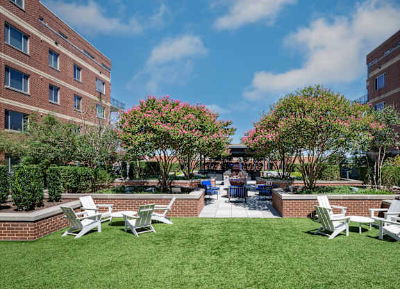 Wide view of The Quad lawn with white Adirondack chairs, landscaped brick planters and apartment buildings on both sides.