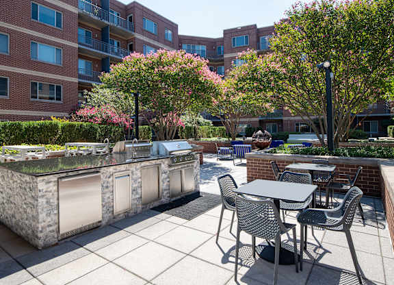 Outdoor grilling area with stone counters, stainless steel grills, black dining furniture and landscaped courtyard views.