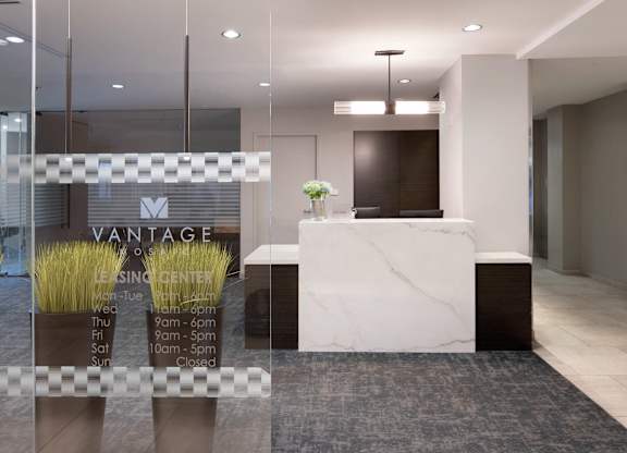 Vantage Mosaic leasing office reception desk viewed through glass doors with the community logo and office hours.