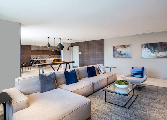Vantage Mosaic resident lounge with a large gray sectional, coffee tables, blue accent pillows and a shuffleboard table.