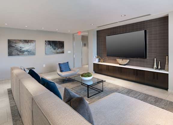 Resident lounge with a gray sectional facing a wall-mounted television and long media console.