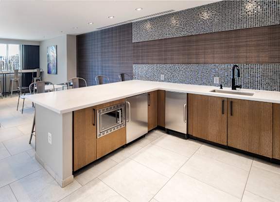 Close view of the resident lounge kitchen with wood cabinets, white countertops, sink, beverage refrigerator and large island.