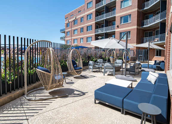 Outdoor Vantage Mosaic patio with hanging egg chairs, blue cushioned seating, small tables and surrounding apartment buildings.