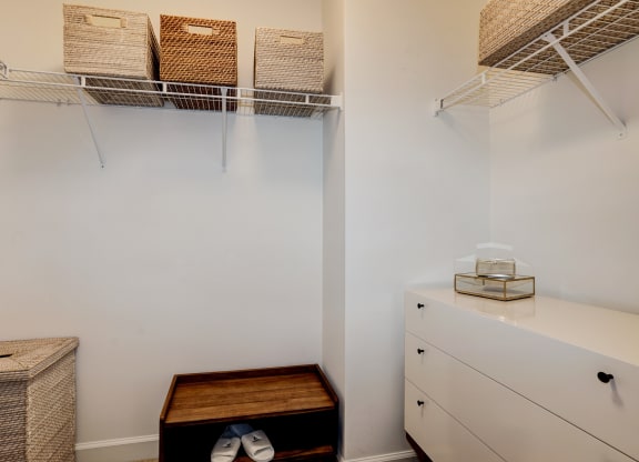 a walk in closet with white walls and shelves and a white dresser with baskets
