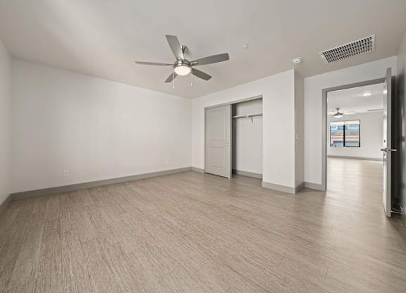 A room with a ceiling fan and light, hardwood floors, and a doorway leading to another room.