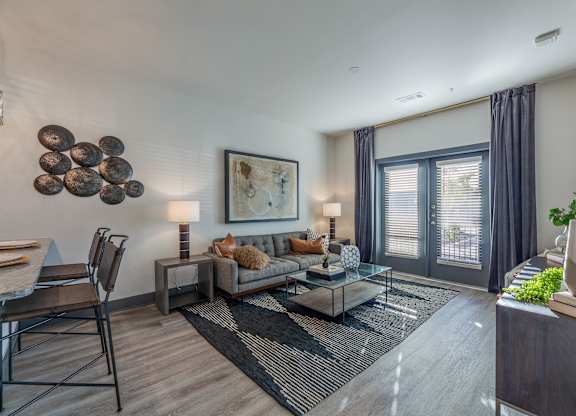 A modern living room with a grey sofa, a glass coffee table, and a large abstract painting on the wall. at Magnolia Grove Apartments, Terrell, Texas