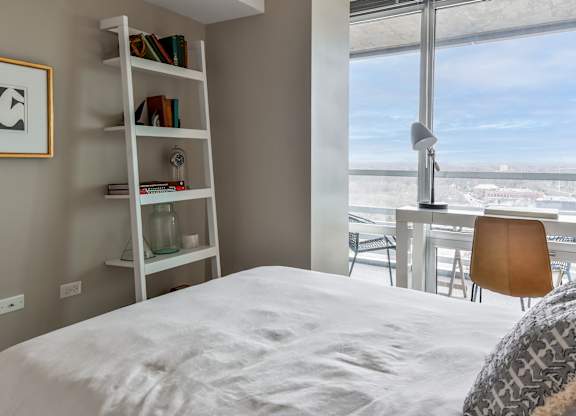 a bedroom with a large bed and a window with a desk and a book shelf at Optima Old Orchard Woods, Skokie, IL, 60077
