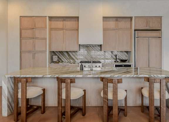 A kitchen with a marble countertop and wooden bar stools.