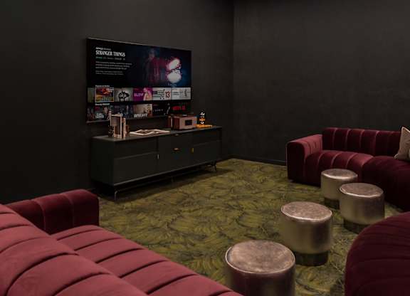 A room with a red couch and ottoman in front of a black wall with a poster on it.