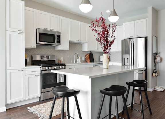 a kitchen with white cabinets and a white island with black stools at The Hallon Apartments, Hopkins, Minnesota