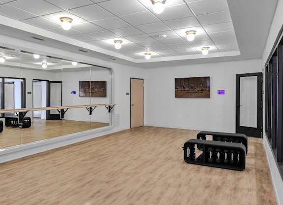 A dance studio with a mirrored wall and wooden flooring.