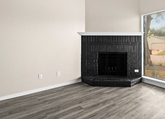 A black fireplace in a room with wooden flooring and a window.