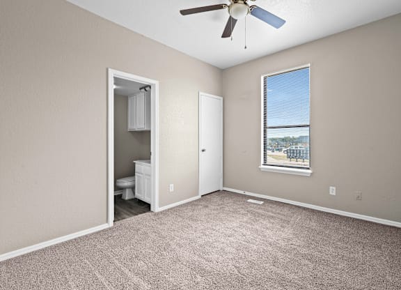 A room with a ceiling fan and a window with a view of a fence and trees.