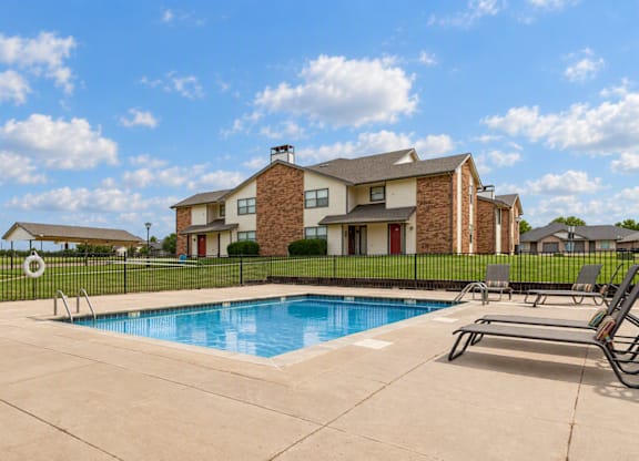 A swimming pool in front of a house with a black fence.