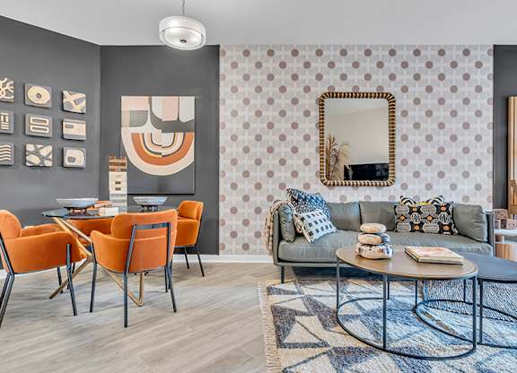A living room with a grey couch, orange chairs, and a patterned wallpaper.