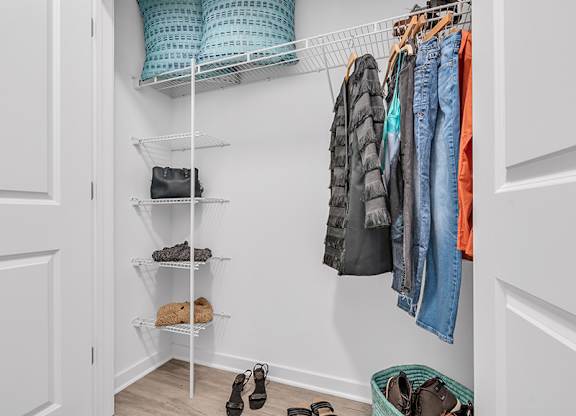 A closet with clothes hanging and shoes on the floor.