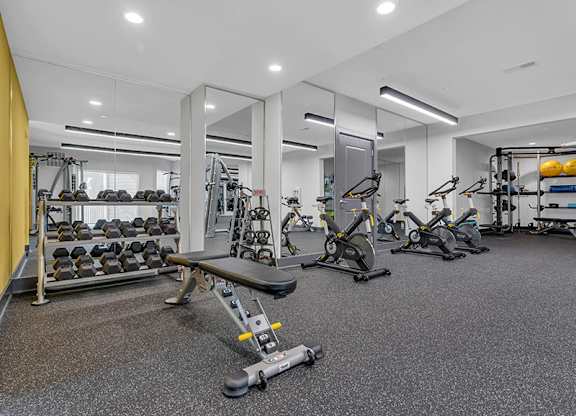 A gym with a variety of equipment including dumbbells, weight machines, and a bench press.