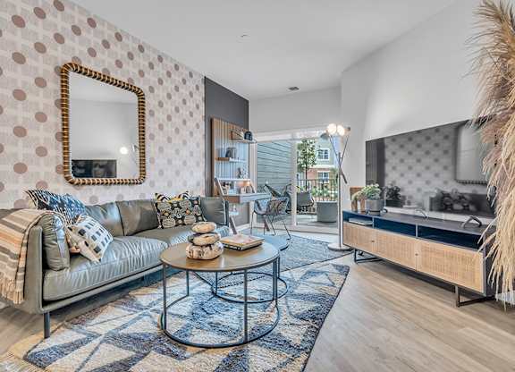 A living room with a grey couch, a round coffee table, and a mirror on the wall.
