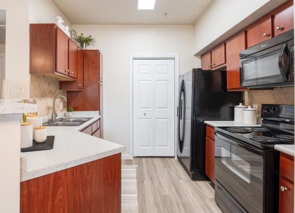 Kitchen with black appliances and wood cabinets at Park Hudson Place Apartments, Bryan, Texas