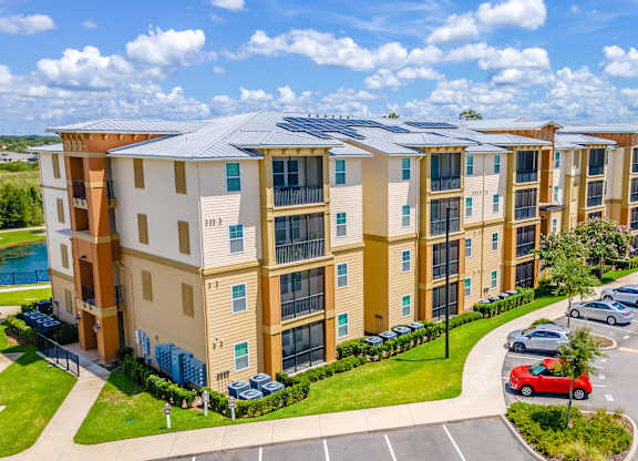 A row of apartment buildings with cars parked in the driveway.
