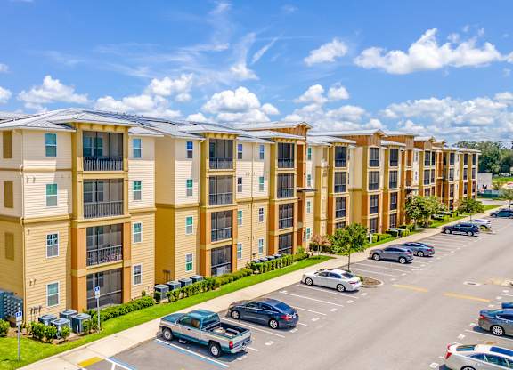 A row of apartment buildings with cars parked in front.