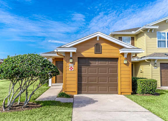 A yellow house with a brown garage door and a tree in front.