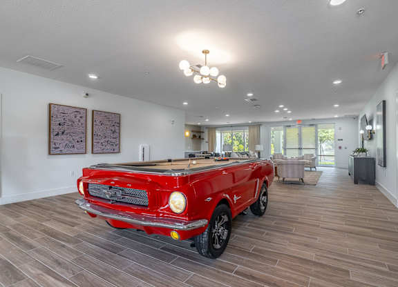 A red vintage car is parked in a spacious room with wood flooring.