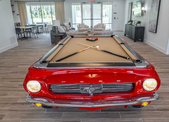A red vintage car is parked in a room with a pool table.