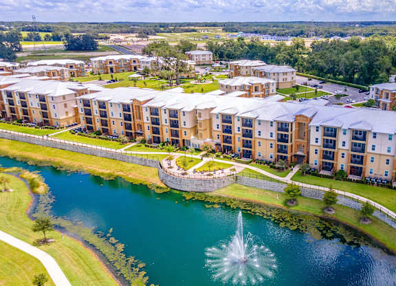 A large apartment complex with a fountain in the middle of a pond.