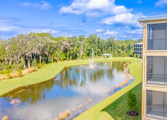 A building is seen from a distance with a fountain in the middle of a pond.