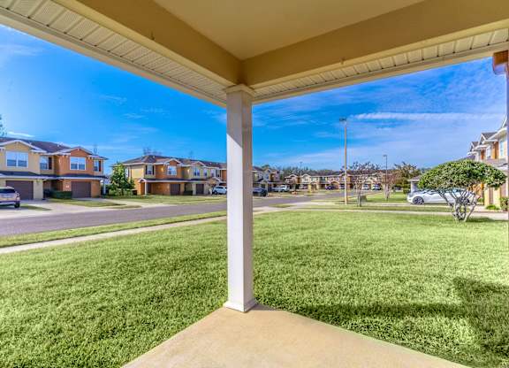 A view from a covered porch looking out at a grassy area and houses.