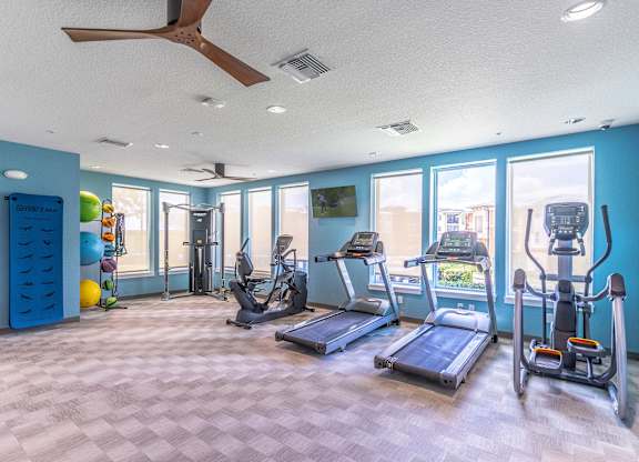 A spacious gym with a variety of equipment including treadmills, elliptical machines, and a fan.