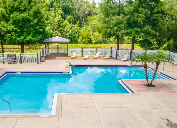 a swimming pool with chairs around it and trees in the background