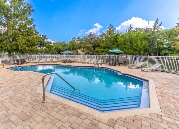 a resort style pool with chairs and umbrellas in a yard with trees