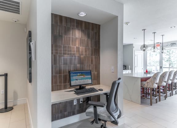 a desk with a computer in a room with a kitchen in the background