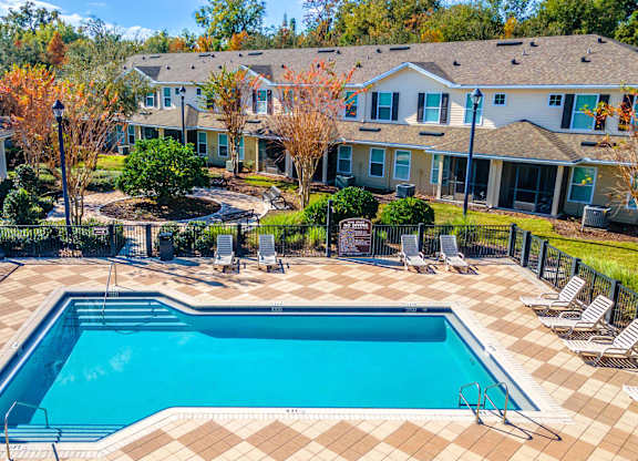 A swimming pool surrounded by a fence and chairs in a residential area.
