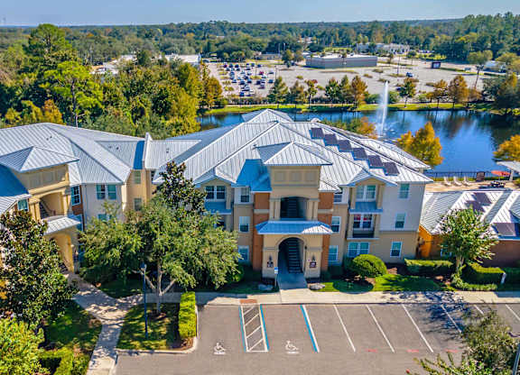 A large building with a blue roof is surrounded by trees and a parking lot.
