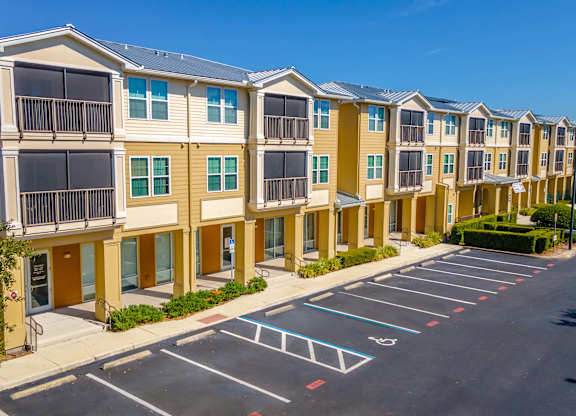 A row of apartment buildings with a parking lot in front.