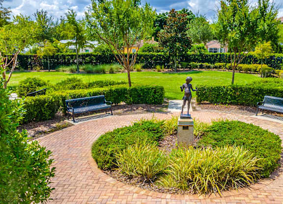 A statue in the middle of a circular brick walkway surrounded by greenery.