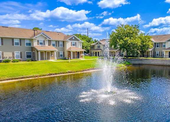 A fountain in the middle of a pond in front of apartment buildings.
