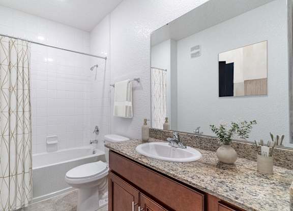 A bathroom with a white toilet, a sink, and a shower with a gold patterned shower curtain.