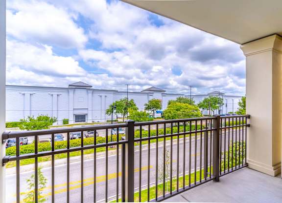 A balcony with a black railing overlooks a street with cars and buildings.