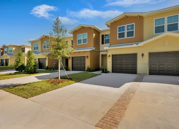 a house with two garages and a tree in the middle of a driveway