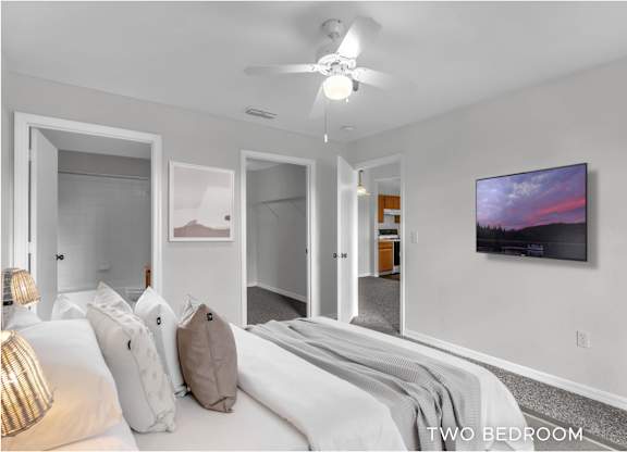 A bedroom with a bed, pillows, a ceiling fan, and a painting on the wall.