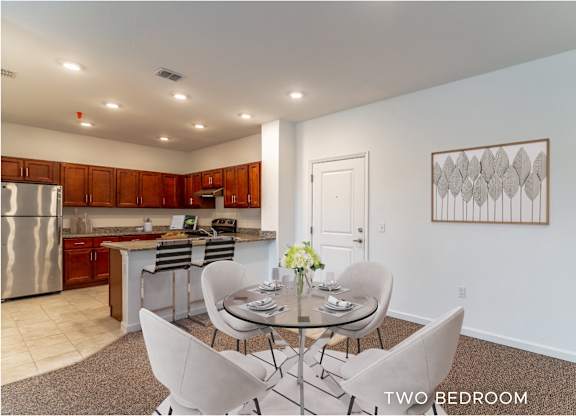 A kitchen with a dining table and chairs in the foreground and a fridge in the kitchen area in the background.