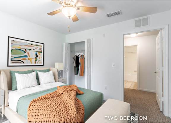 A bedroom with a bed, a ceiling fan, and a painting on the wall.