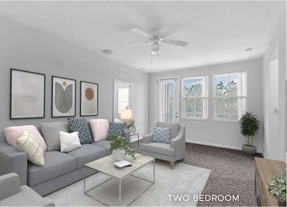 A living room with a grey couch, a glass coffee table, and a ceiling fan.