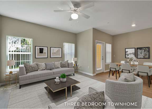 A well-lit, spacious living room with a grey sofa, a coffee table, and a dining area with a table and chairs.