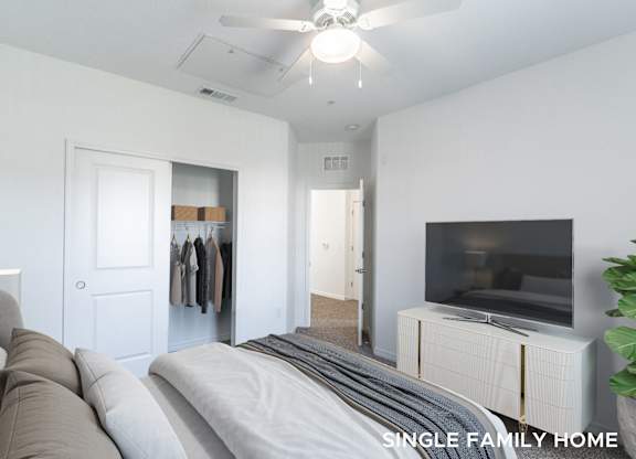 A bedroom with a grey bed and a television on a dresser